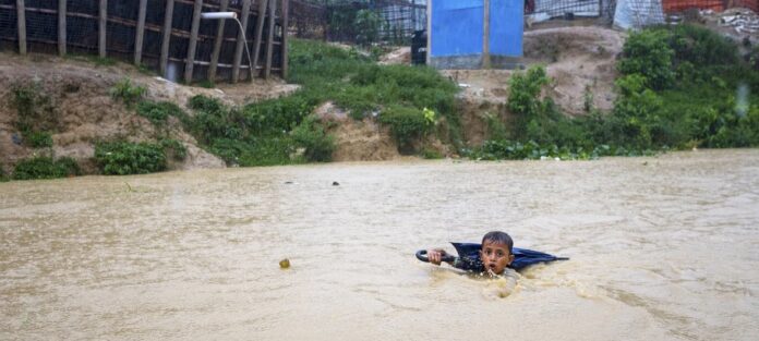 Um menino em Bangladesh navega em um rio cheio devido aos dias de chuva de monções. Ele está coletando garrafas plásticas jogadas no rio para vender a recicladores e ajudar sua família a comprar alimentos
